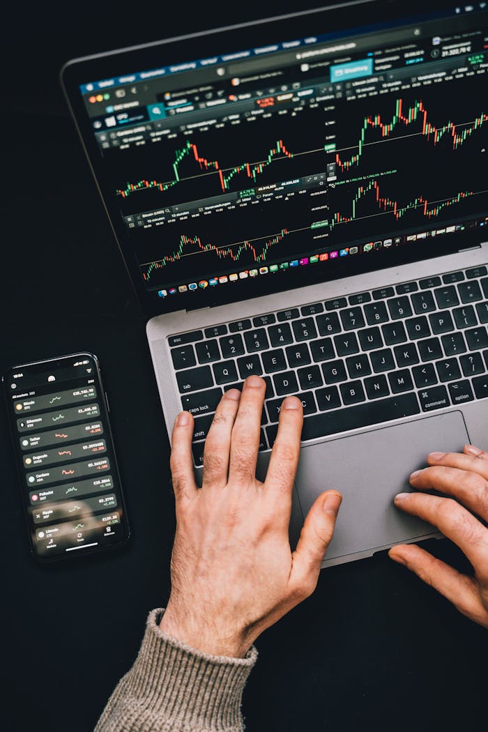 services-02 Hands typing on a laptop with cryptocurrency charts and smartphone display in view, focusing on digital finance.