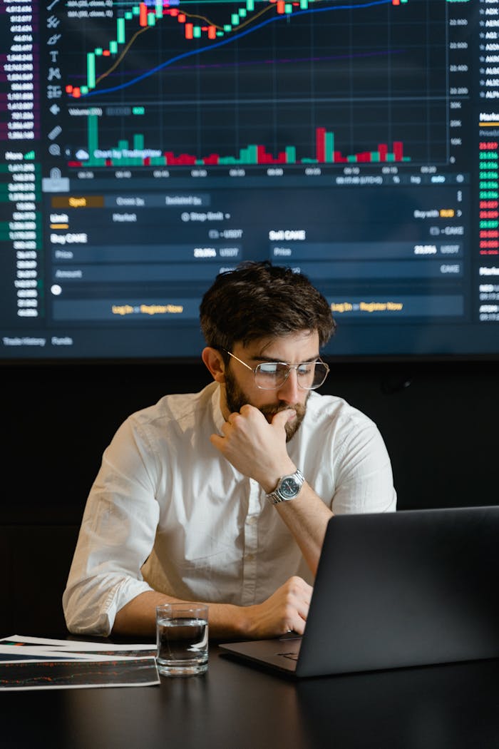 who-we-are Pensive businessman with a beard analyzing stock market trends on a laptop in an office setting.