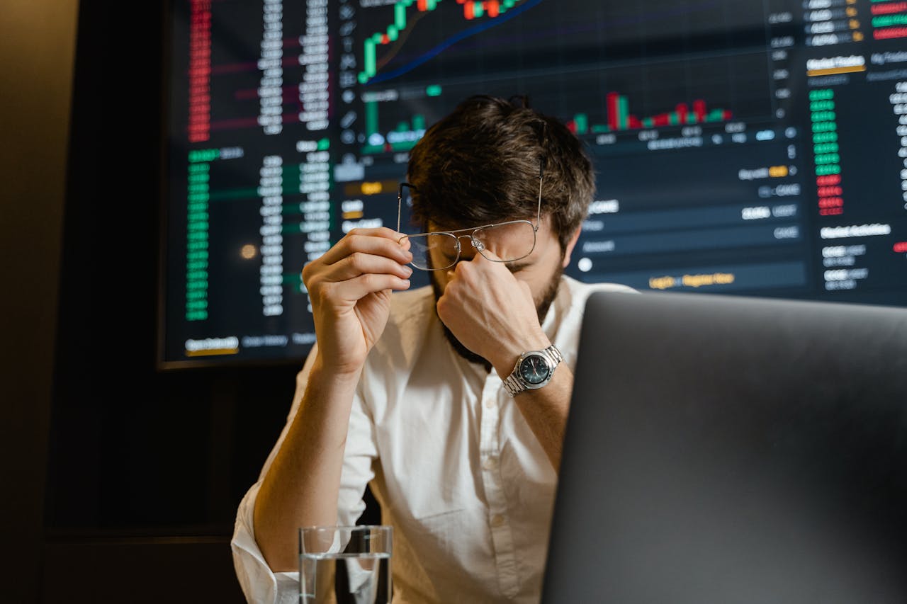 our-story A stressed man looks at stock market data on his computer screen in an office setting.