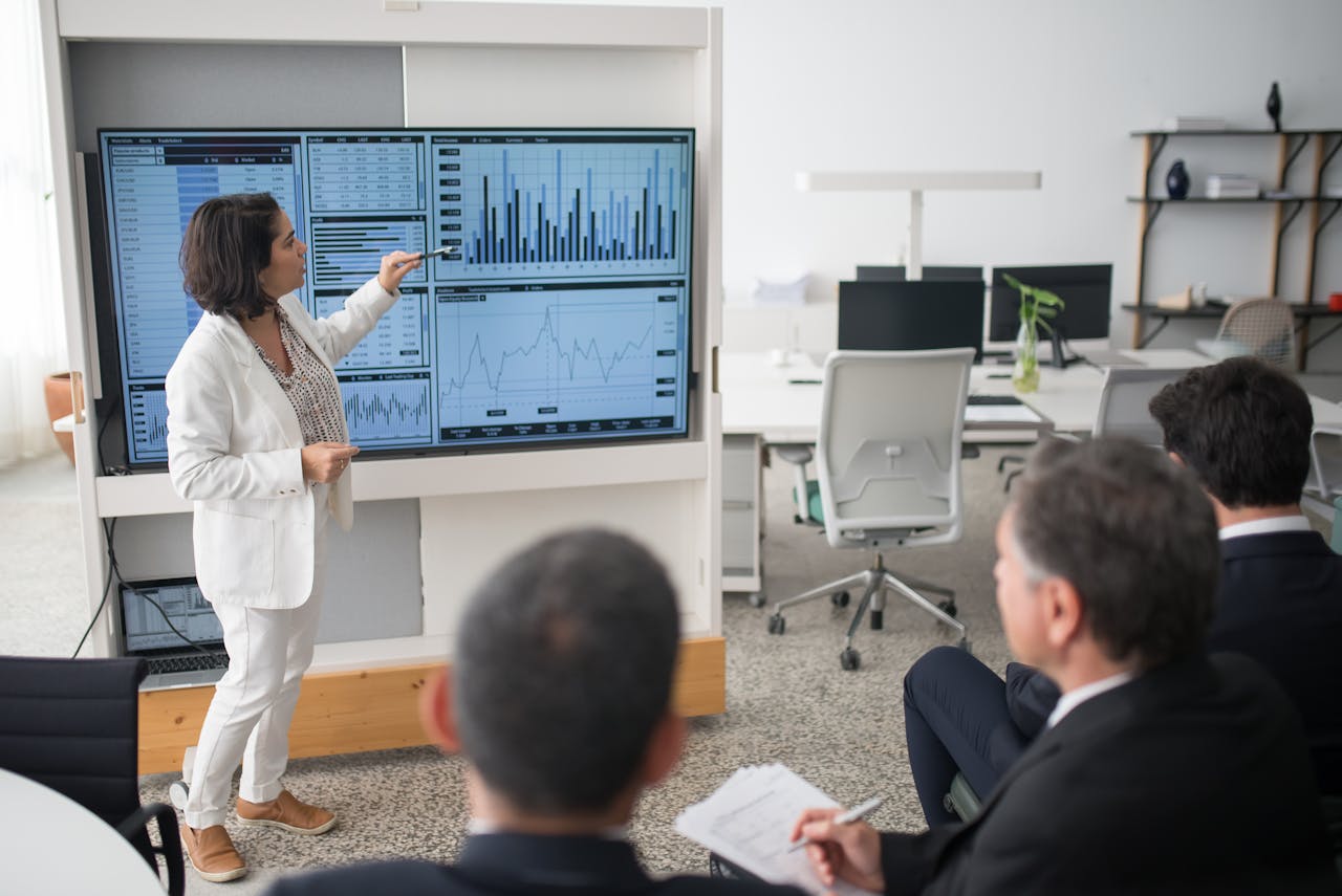 about-us A woman presents data on a screen to a group of colleagues in an open office environment.